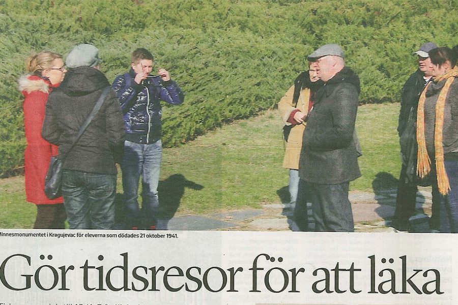 Sex människor står utomhus vid minnesmonumentet i Kragujevac, Belgrad. De är varmt klädda och en av dem tar en bild. Under bilden finns texten “Minnesmonumentet i Kragujevac för eleverna som dödades 21 oktober 1941.”