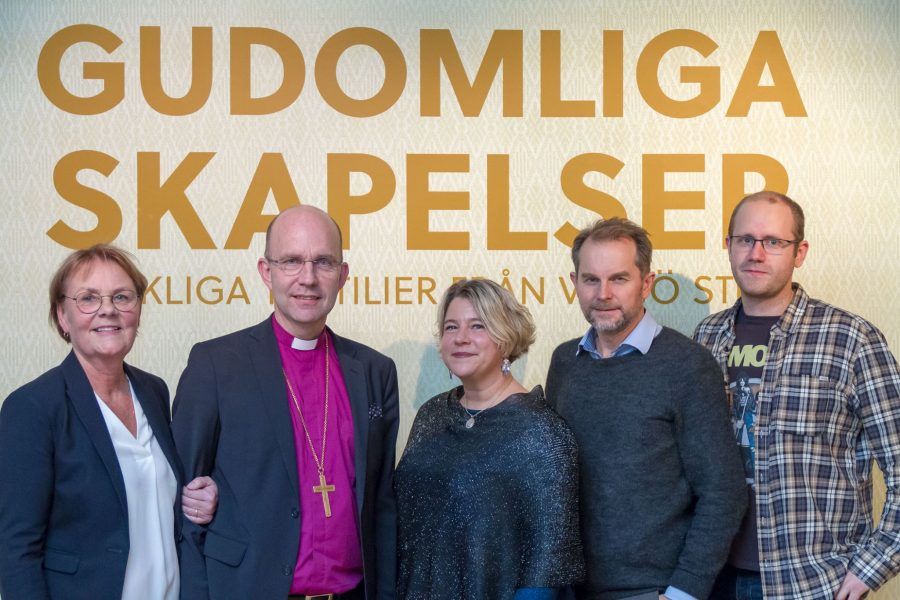 Fem personer står framför en bakgrund med texten "Gudomliga skapelser, verkliga familjer från Växjö stift." En man i prästkläder står i mitten och bär ett korshalsband. Personen till vänster har glasögon.