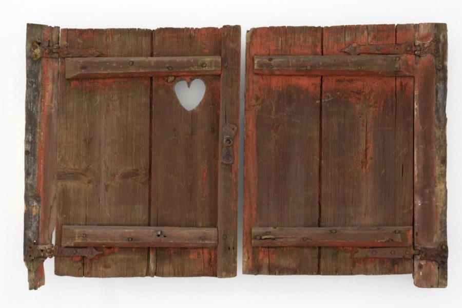 Gamla, slitna träfönsterluckor med rödbrun färg och patina. Luckorna har en hjärtformad utskärning på ena sidan. Rester av metallbeslag syns vid kanterna. Luckornas yta är ojämn och åldrad.