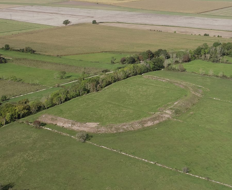 Flygbild över en halvfärdig borg omgiven av vidsträckta åkrar och skogsdungar. Jordmassan bildar en tydlig kurva med omgivande grönska. Fälten sträcker sig bortåt horisonten, vilket ger en vy över det öppna landskapet.